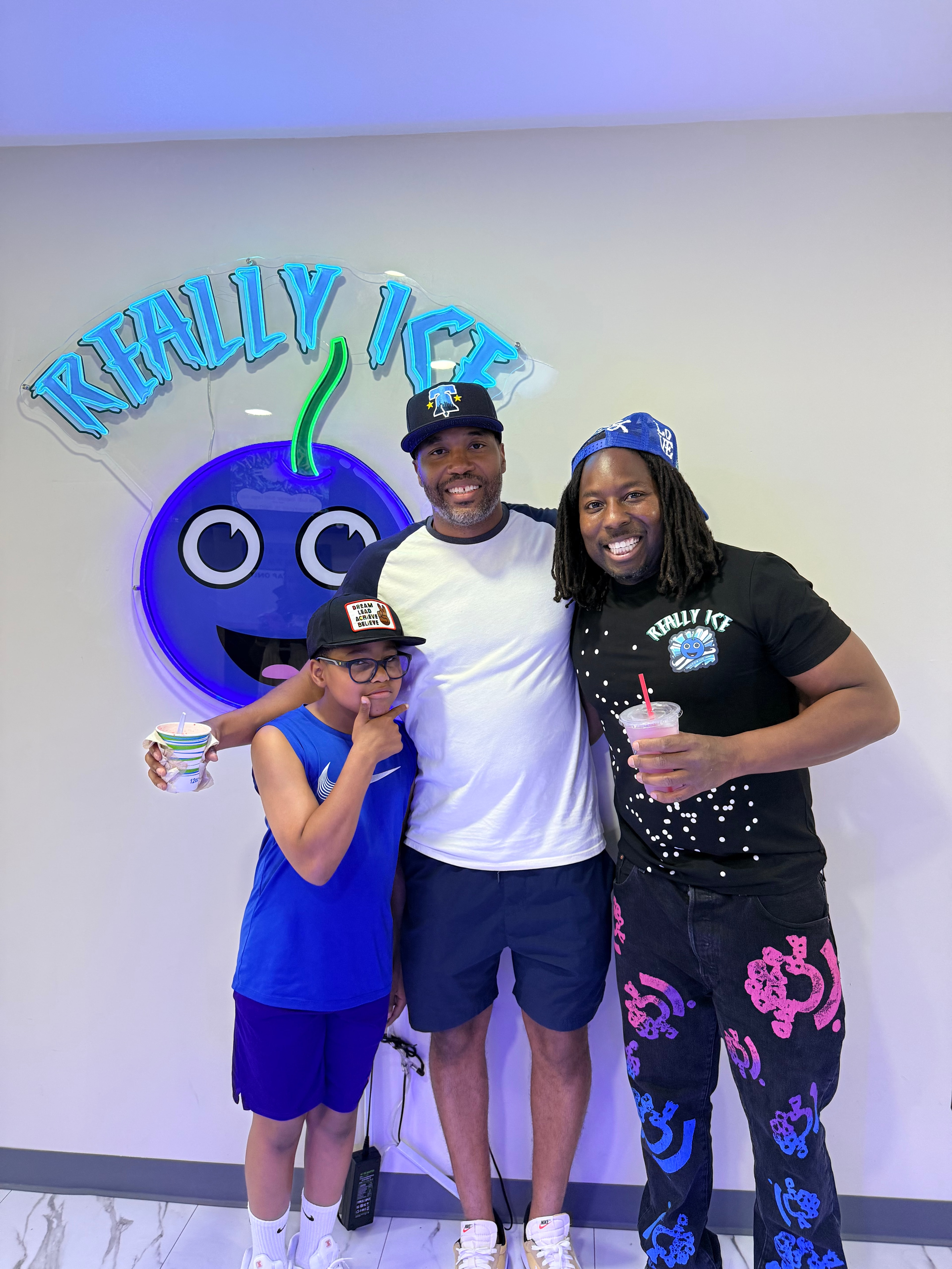 Three visitors posing with the Really Ice mascot logo on the wall